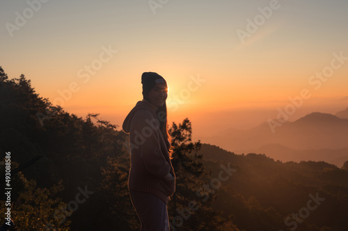 Happy asian woman wearing beanie standing with sunrise over mountain in the morning © Mumemories