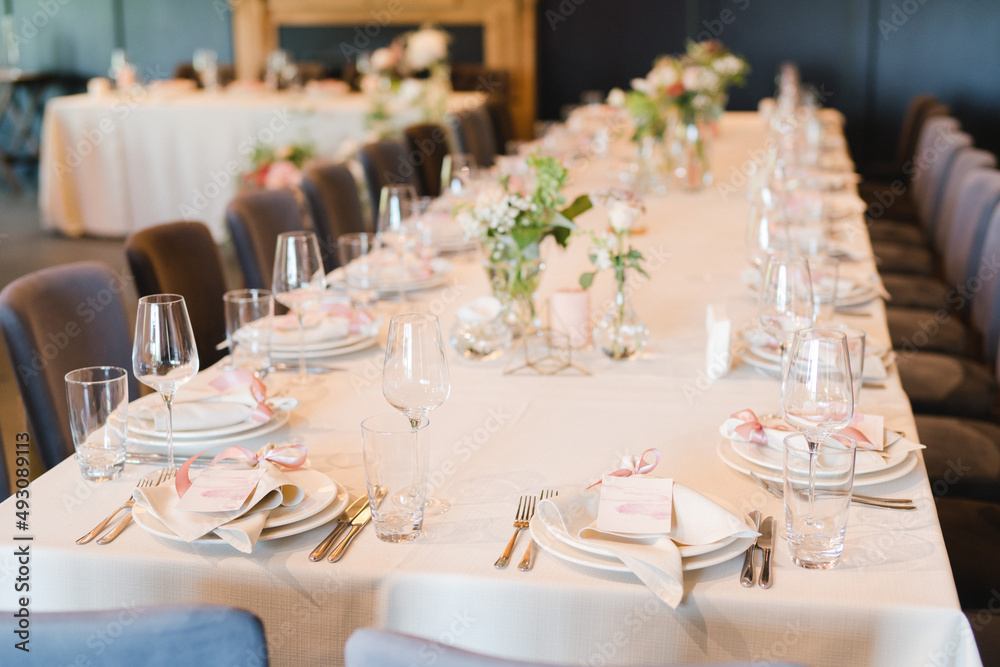 Coziness and style. Modern event design. Table setting at wedding reception. Floral compositions with beautiful flowers and greenery, candles, laying and plates on decorated table. Coziness and style. Modern event design. Table setting at wedding reception. Floral compositions with beautiful flowers and greenery, candles, laying and plates on decorated table.