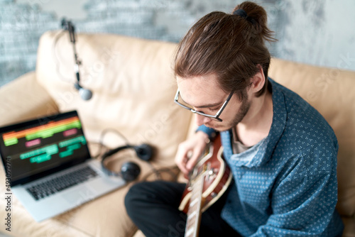 Learning to play the guitar at home, a free guy on a leather sofa playing the guitar