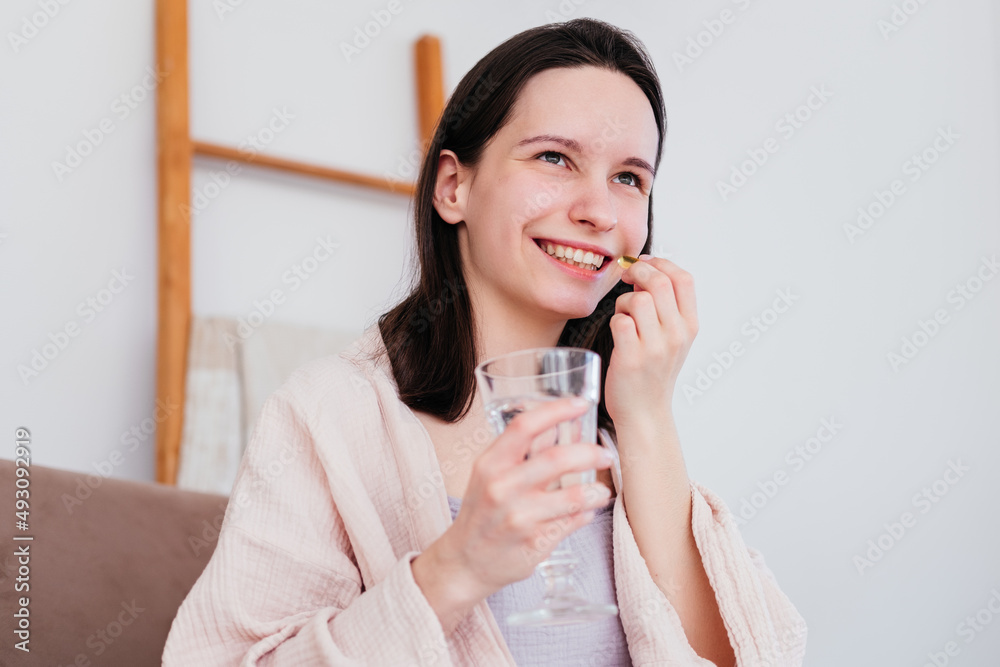Smiling young woman holding pill and glass of water in hand at home. Girl taking medicine Smiling young woman holding pill and glass of water in hand at home. Girl taking medicine