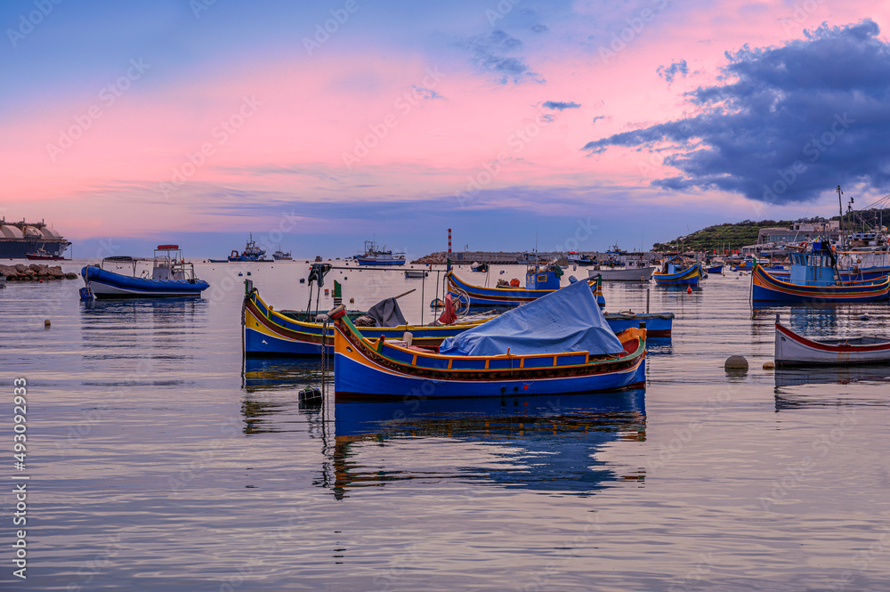 Traditional Maltese boats in Marsaxlokk harbor during sunset, Malta