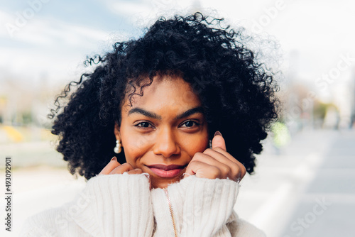 Portrait of a woman smiling at the camera. Attractive young adult woman with afro hair, happy outdoors.