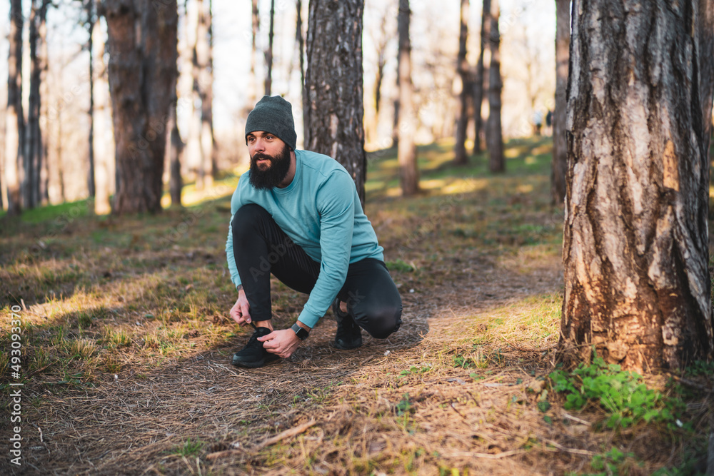 Young sporty man is tying shoelace in nature.
