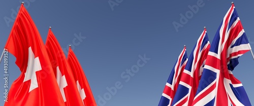Three flags of United Kingdom and Switzerland on flagpoles on sides. Flags on a blue background. Place for text. Great Britain, London. Bern. Commonwealth. 3D illustration.