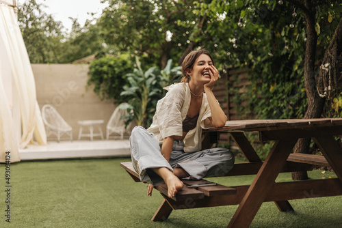 Obraz na plátně Cheerful young caucasian brunette lady is sitting on bench at table in backyard