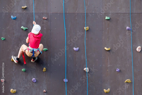 child rock climber holding onto a rope at a climbing training stand