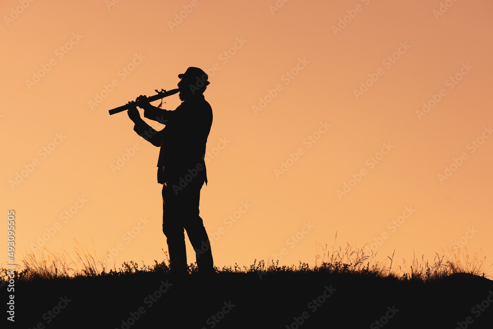 silhouette of a man in a hat playing the flute. musician in nature outdoors against the backdrop of sunset