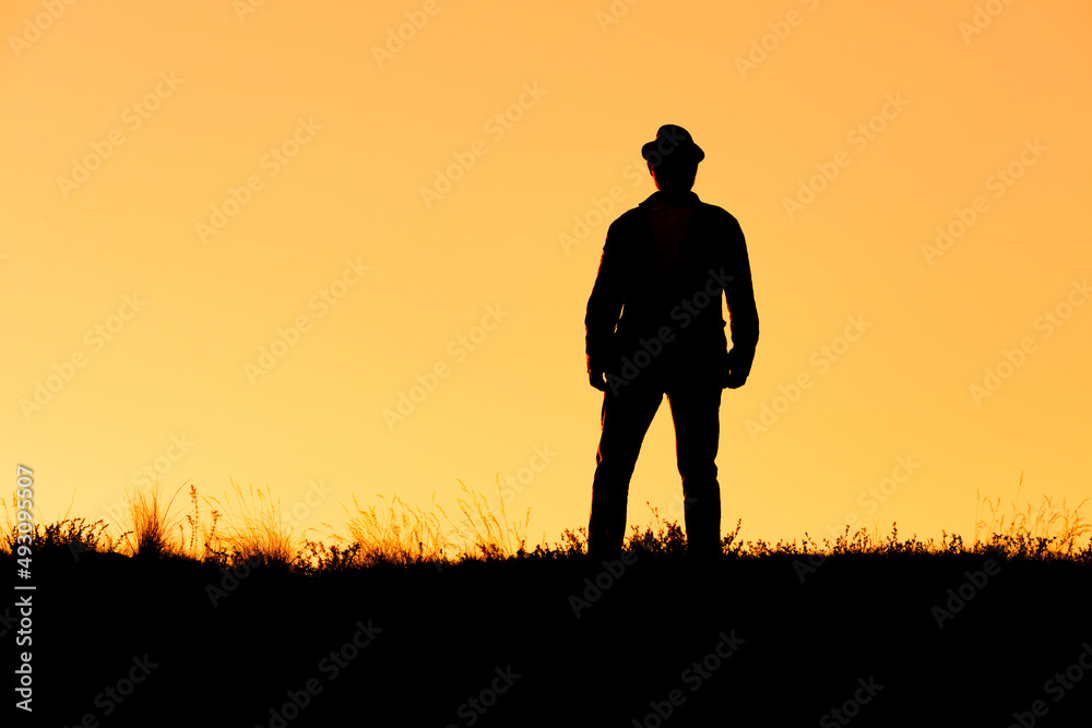 silhouette of a standing man in a hat on an orange background
