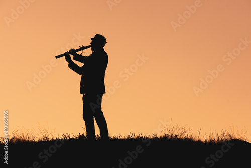 silhouette of a man in a hat playing the flute. musician in nature outdoors against the backdrop of sunset