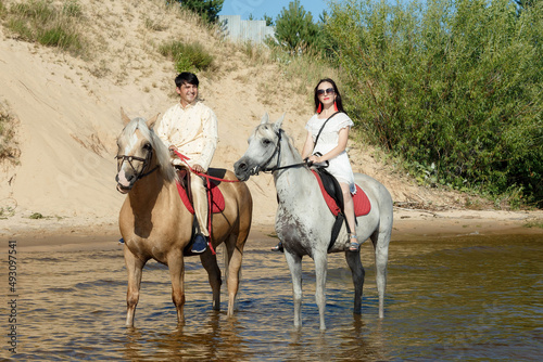 a guy and a girl on horseback on a river on a sunny day © artem