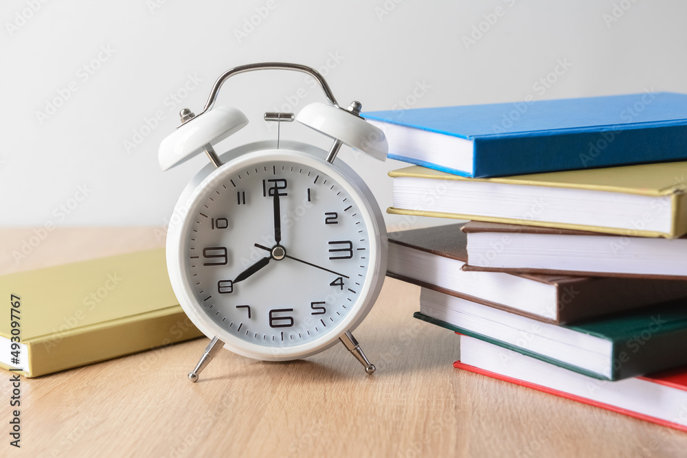 Stack of books and alarm clock on table, closeup