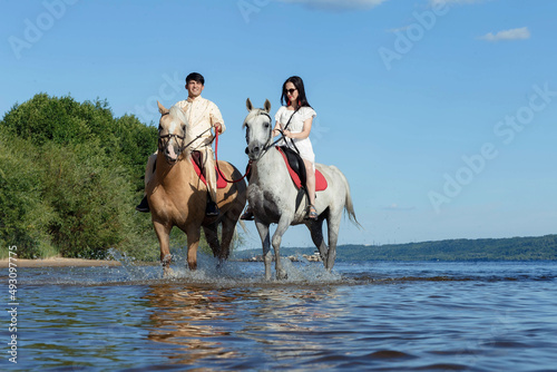 a guy and a girl on horseback on a river on a sunny day