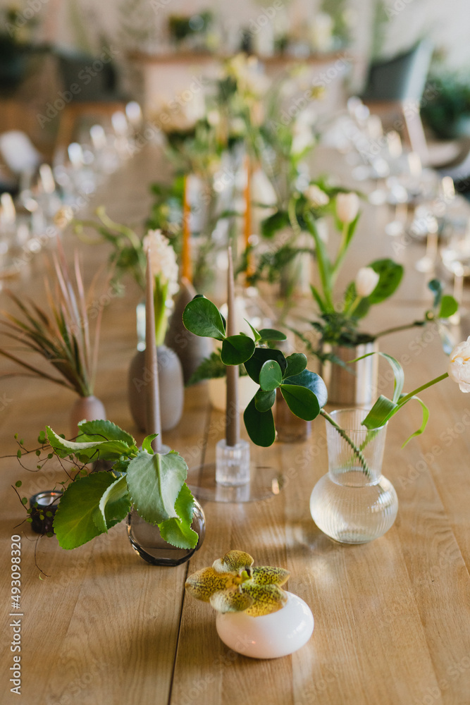 Coziness and style. Modern event design. Table setting at wedding reception. Floral compositions with beautiful flowers and greenery, candles, laying and plates on decorated table. Coziness and style. Modern event design. Table setting at wedding reception. Floral compositions with beautiful flowers and greenery, candles, laying and plates on decorated table.