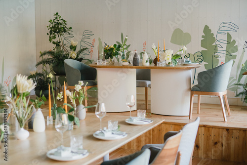 Coziness and style. Modern event design. Table setting at wedding reception. Floral compositions with beautiful flowers and greenery, candles, laying and plates on decorated table. © anna_gorbenko