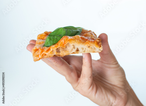 A hand holding a slice of Italian style pizza al taglio