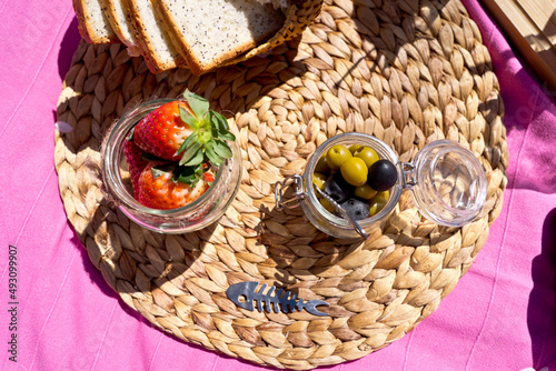 Horizontal top view of picnic with strawberries and olives outdoors. Above shot of variety of snack food set with wicker blanket background. Gastronomy and food concept.