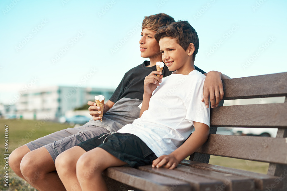 You cant be sad when youre eating ice-cream. Shot of two happy brothers eating ice-cream cones while sitting on a bench by the beach.