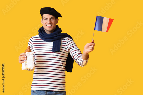 Handsome young man with flag of France and croissants on yellow background photo