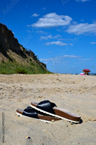In the foreground are women's sandals on a sandy beach. The background is blurry © Serhii
