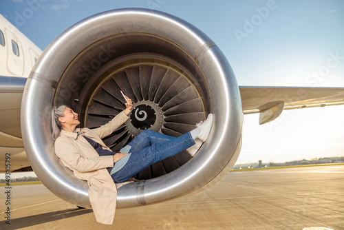 Cheerful woman lying in aircraft engine and doing selfie