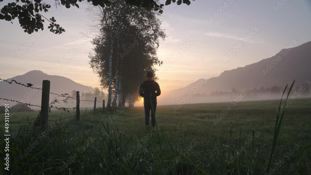 Man Walking Through Meadow Towards Foggy Landscape And Sunrise Man Walking Through Meadow Towards Foggy Landscape And Sunrise