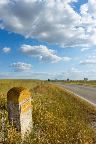 PAISAJE DE CARRETERA CON PUNTO KILOMÉTRICO Y FONDO CON CIELO AZUL Y NUBES