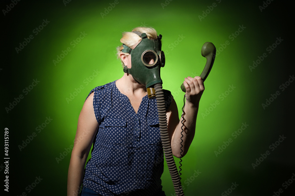 Funny woman in a gas mask looks in surprise at the handset of a retro phone  on a dark background, hard light. Stock Photo | Adobe Stock