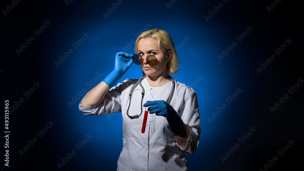 Fototapeta premium A female doctor in a white coat, gloves and glasses with a test tube of blood in her hands on a dark background, hard light. The concept of laboratory research under sanctions.
