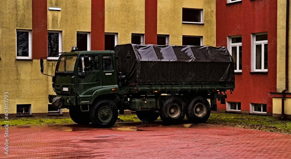 Naklejka premium Wojskowa ciężarówka terenowa ( of road ) polskiej produkcji , Star 266 , z plandeką , w kolorze khaki , parkująca przed budynkiem , na powierzchni brukowanej kostką betonową , w strugach deszczu .