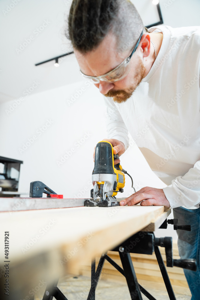 carpenter in protective glasses cuts wood with electric jigsaw