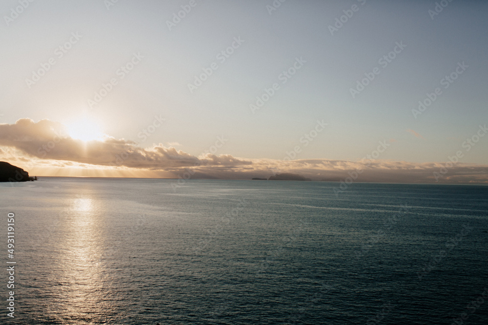 Picture of blue blue calm ocean at sunset. Landscape of ocean with low clouds and sun Picture of blue blue calm ocean at sunset. Landscape of ocean with low clouds and sun