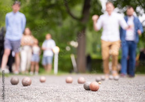 Friends playing petangue outdoor game balls in the foreground on court in summer city park	
