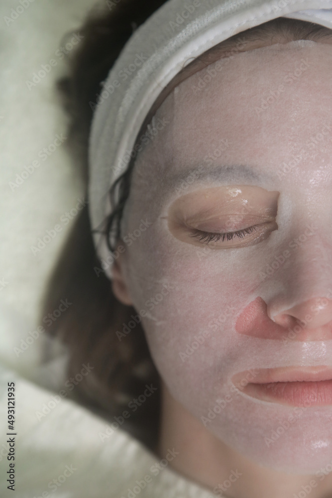 Woman with facial sheet mask relaxing at beauty salon. Skin care concept. 