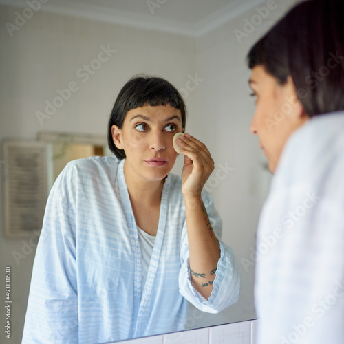 Shes perfected her morning routine. Shot of a young woman in a bathrobe applying foundation in her bathroom mirror in the morning.
