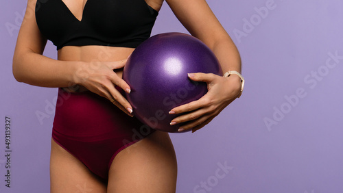 Unrecognizable fit woman in top and high waist panties with pilates ball. Faceless healthy slim female girl has sporty body posing over lilac background. Healthy lifestyle. Beauty and health care