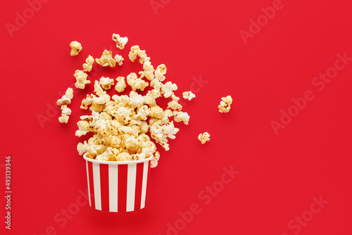 Striped round box with popcorn on a bright red background. Flat lay, copy space