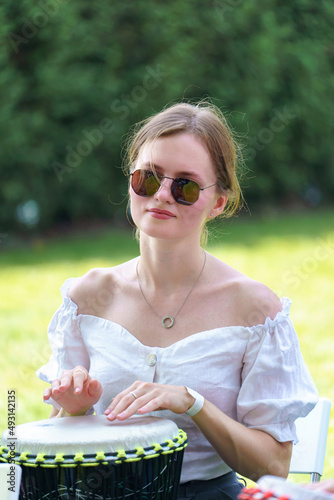 Beautiful girl in sunglasses and a white blouse plays the drum outdoor
