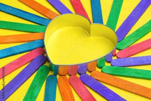 Colorful wooden sticks for DIY school crafts concentrically arranged around a heart shaped cookie cutter photo