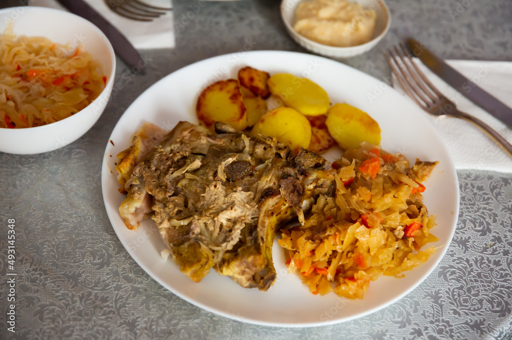 Portion of baked pork meat with roasted potatoes and stewed cabbage.