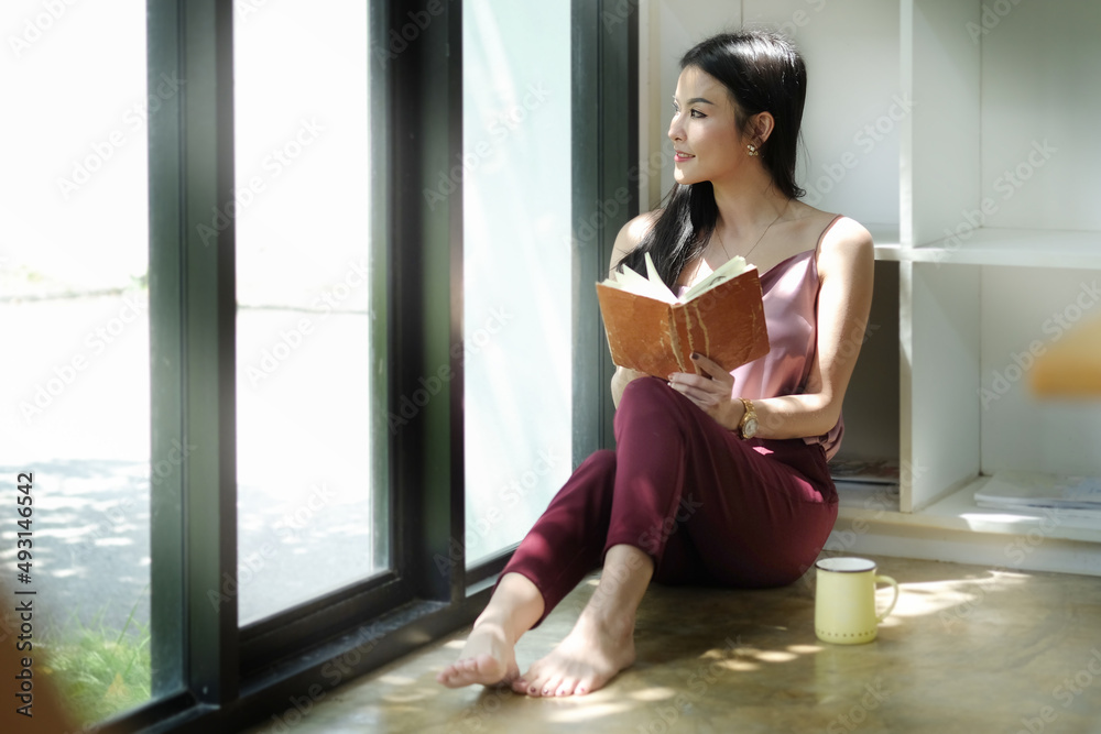Peaceful asian woman sitting on floor in bright living room and looking out of window. Peaceful asian woman sitting on floor in bright living room and looking out of window.
