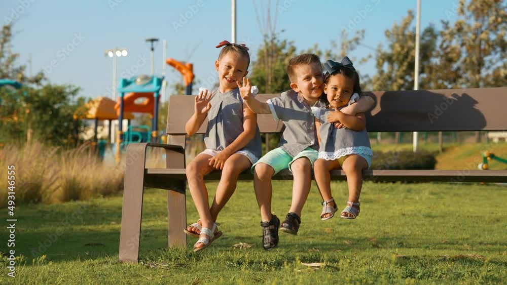 Niños Felices amigos hermanos combinados vestidos igual amistad divertidos disfrutando sentados jugando en el parque en una banca al aire libre en juegos infantiles
