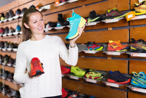 Portrait of young cute woman choosing sneakers in sports store