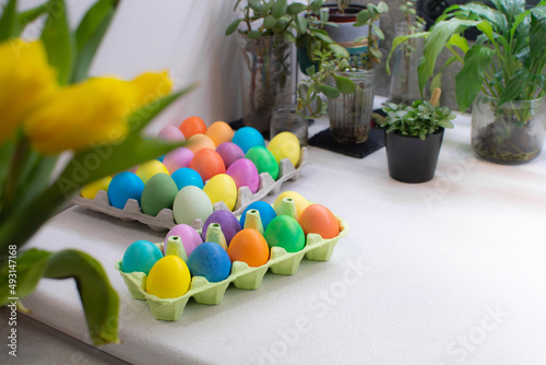 Many colorful Easter eggs in carton box on table in kitchen interior