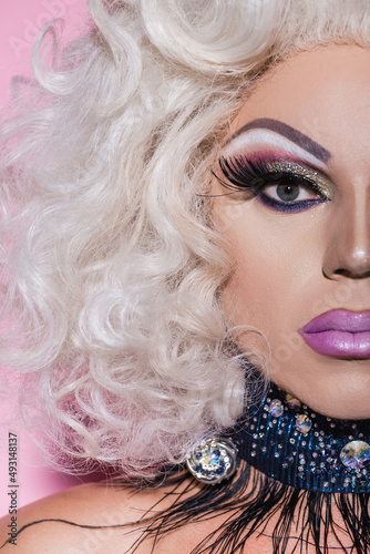 close up portrait of cropped drag queen with bright makeup looking at camera on pink. photo