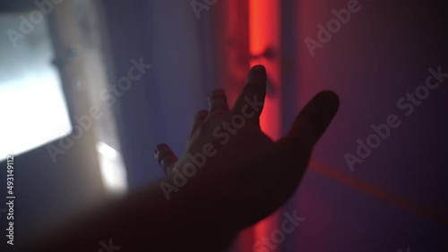 Concept of opening door to the hell, hand of murderer approaching to the room door and slowly opening, horrible scene of room with red lighting, fog and obscure chaos and garbage. Scary crime in dark photo