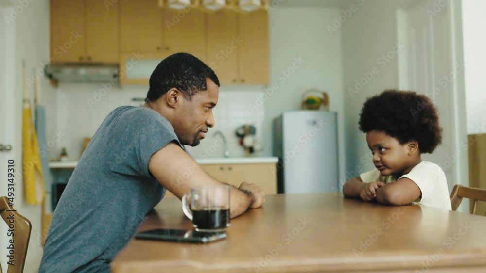 Black African American father teaching arm wrestling with his little boy in kitchen at home Black African American father teaching arm wrestling with his little boy in kitchen at home