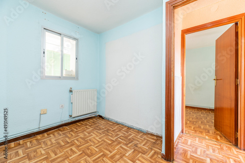 Empty room with wooden parquet, blue painted walls, aluminum window and mahogany colored woodwork