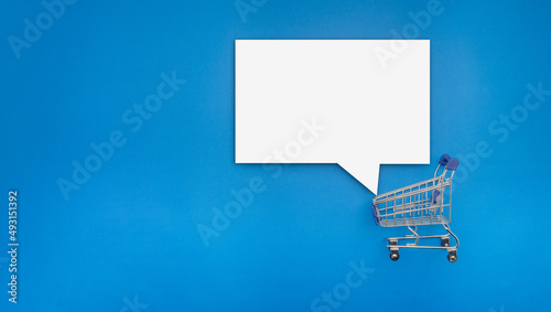 Empty white speech bubble on a mini shopping trolley over blue background