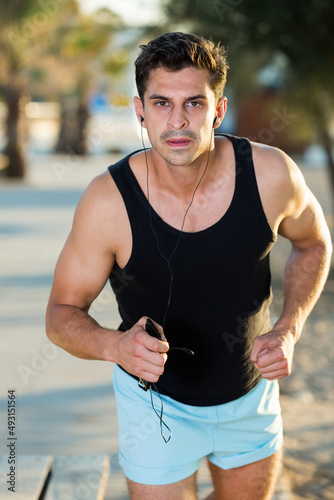 Active concentrated man running along embankment in sunny morning