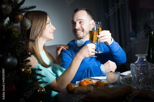 Smiling loving couple celebrating New Year, giving toasts and enjoying dinner at home